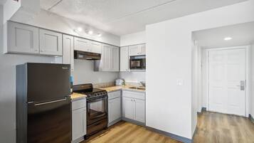 Una cocina moderna con armarios blancos, un refrigerador de acero inoxidable, un microondas y un horno empotrado.