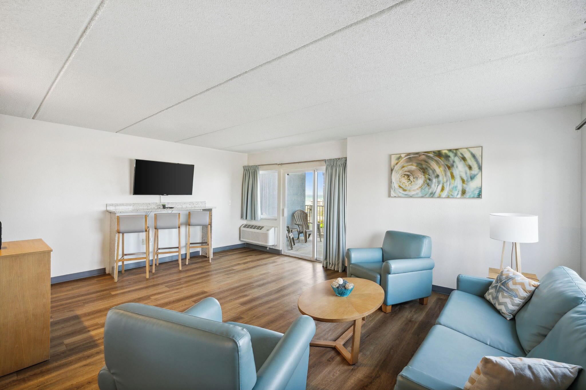 A modern living room with a TV, a dining area with bar stools, a sofa, and a painting on the wall.