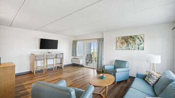 A modern living room with a TV, a dining area with bar stools, a sofa, and a painting on the wall.