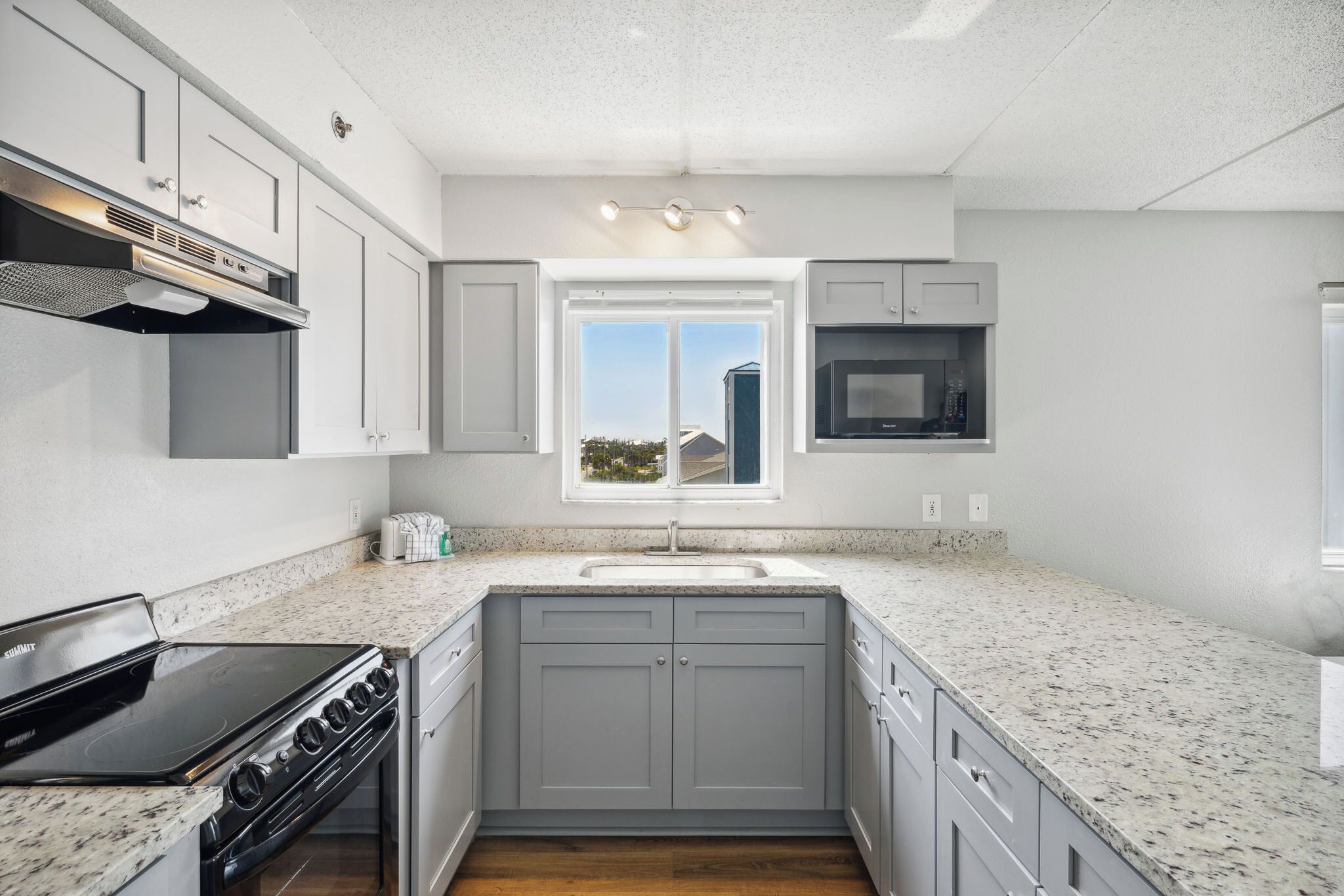 A modern kitchen with grey cabinets, a built-in oven, a microwave, and a window with a view.