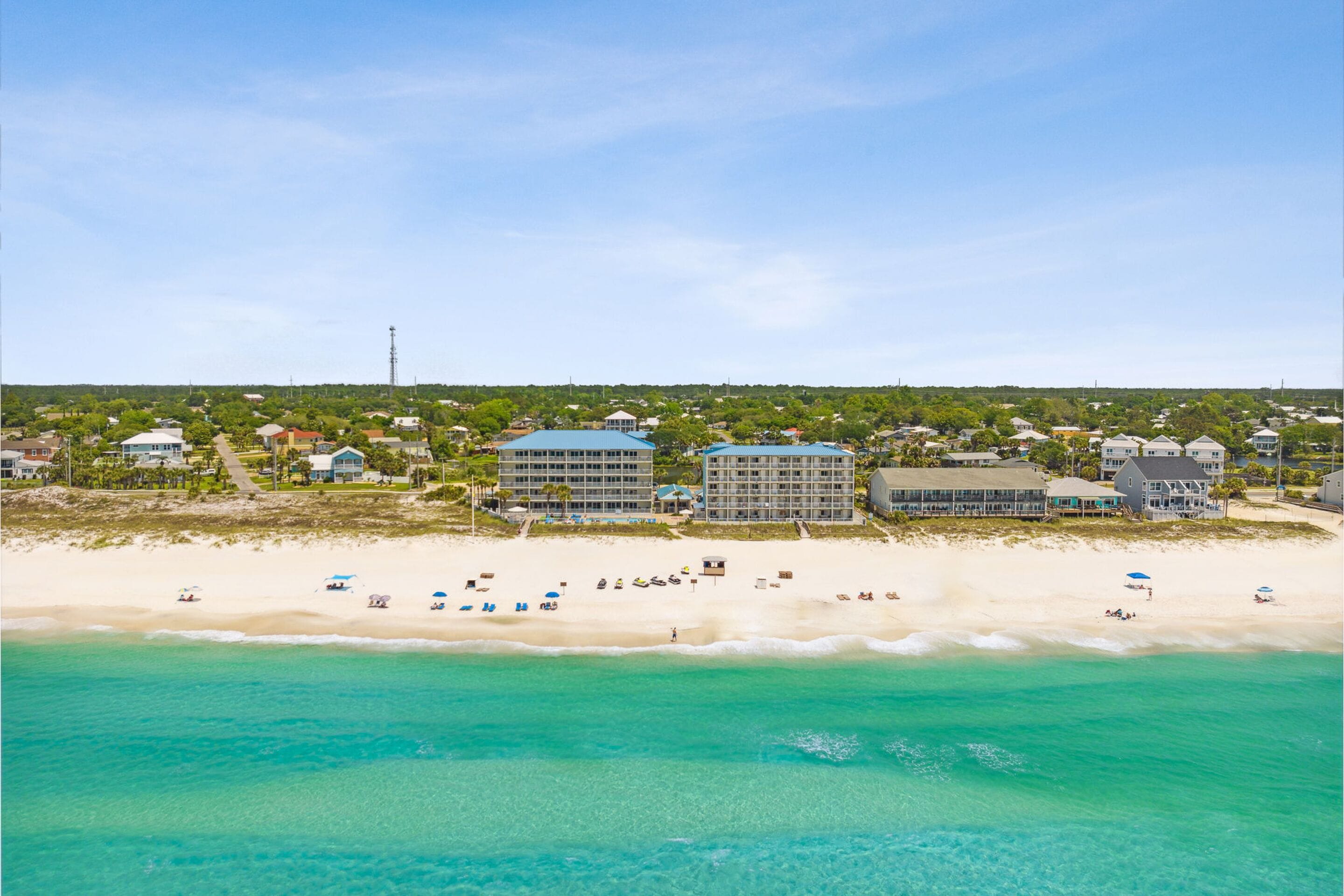 A coastal hotel with multiple buildings, a sandy beach, and clear turquoise waters.
