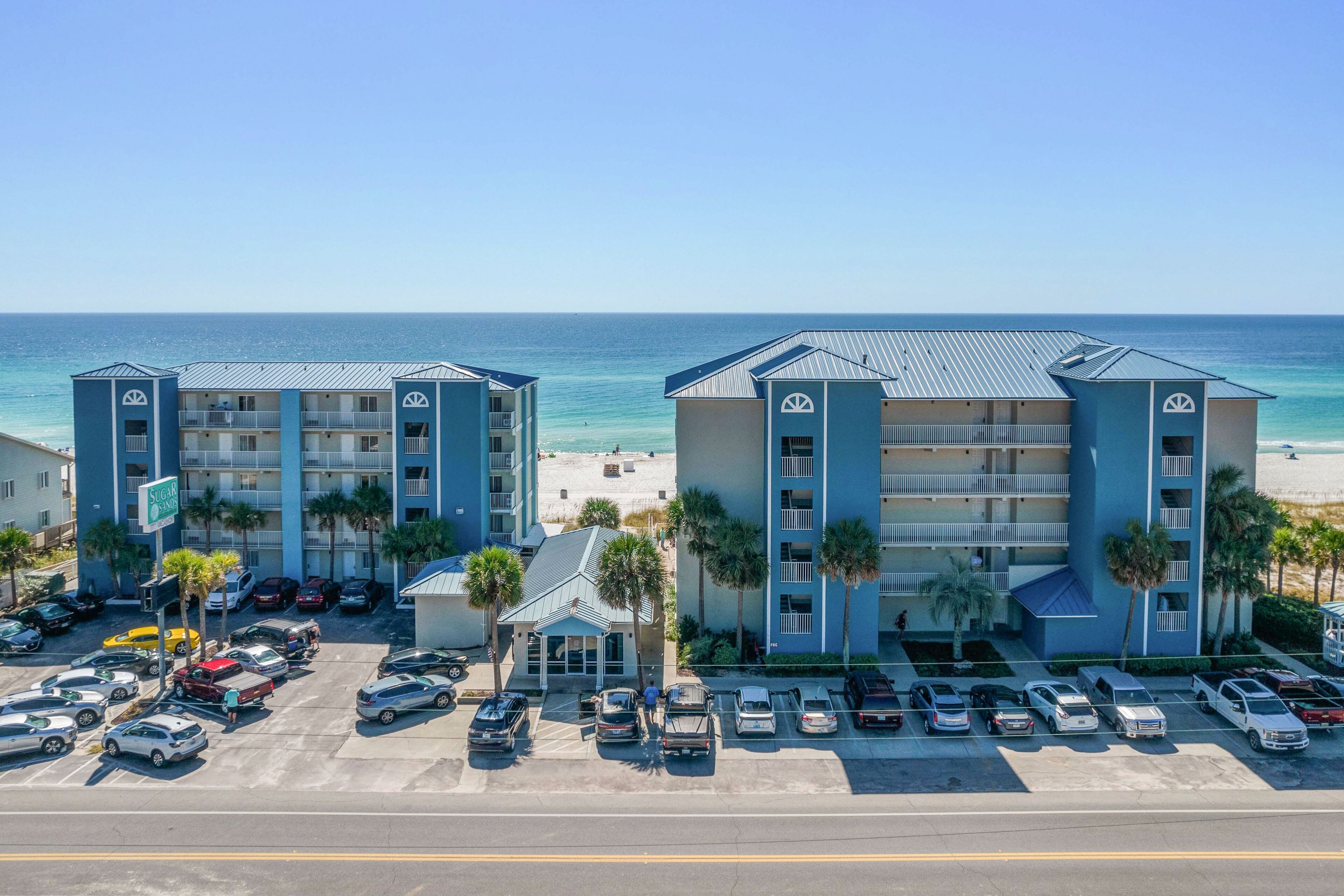 Un hotel frente a la playa con varios balcones, estacionamiento y vistas al océano.