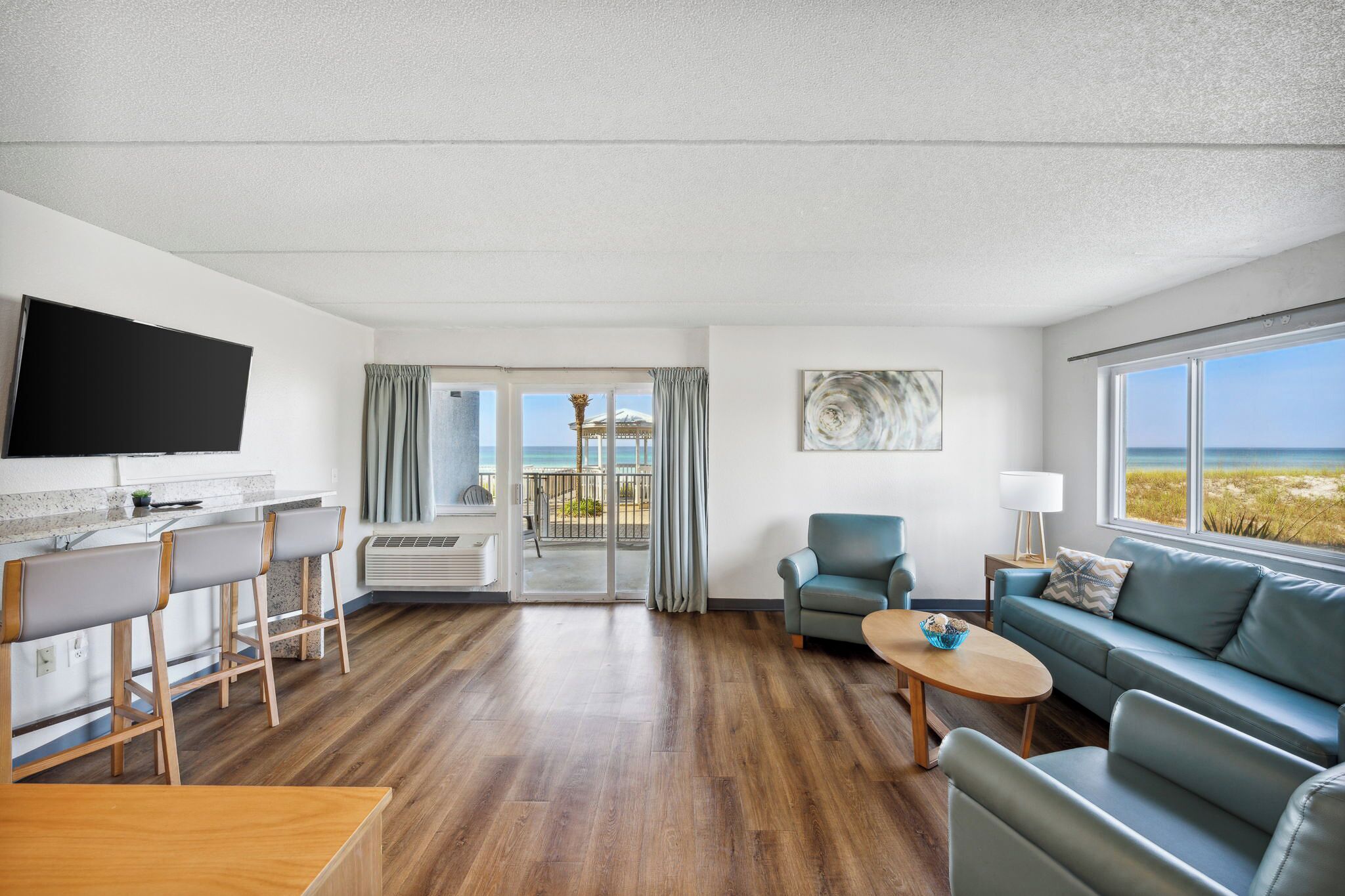Habitación de hotel moderna con cocina, comedor, sofá y balcón con vistas a la playa.