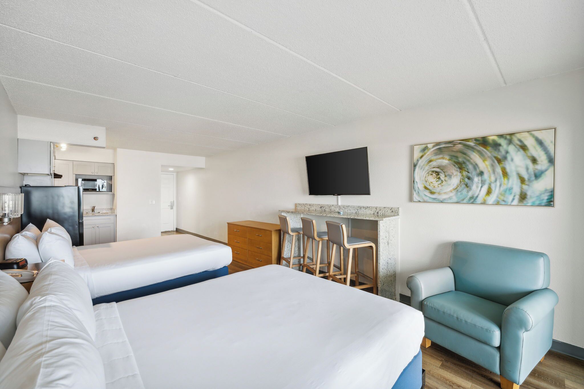 A hotel room with two beds, a kitchenette, a TV, and a bar area.