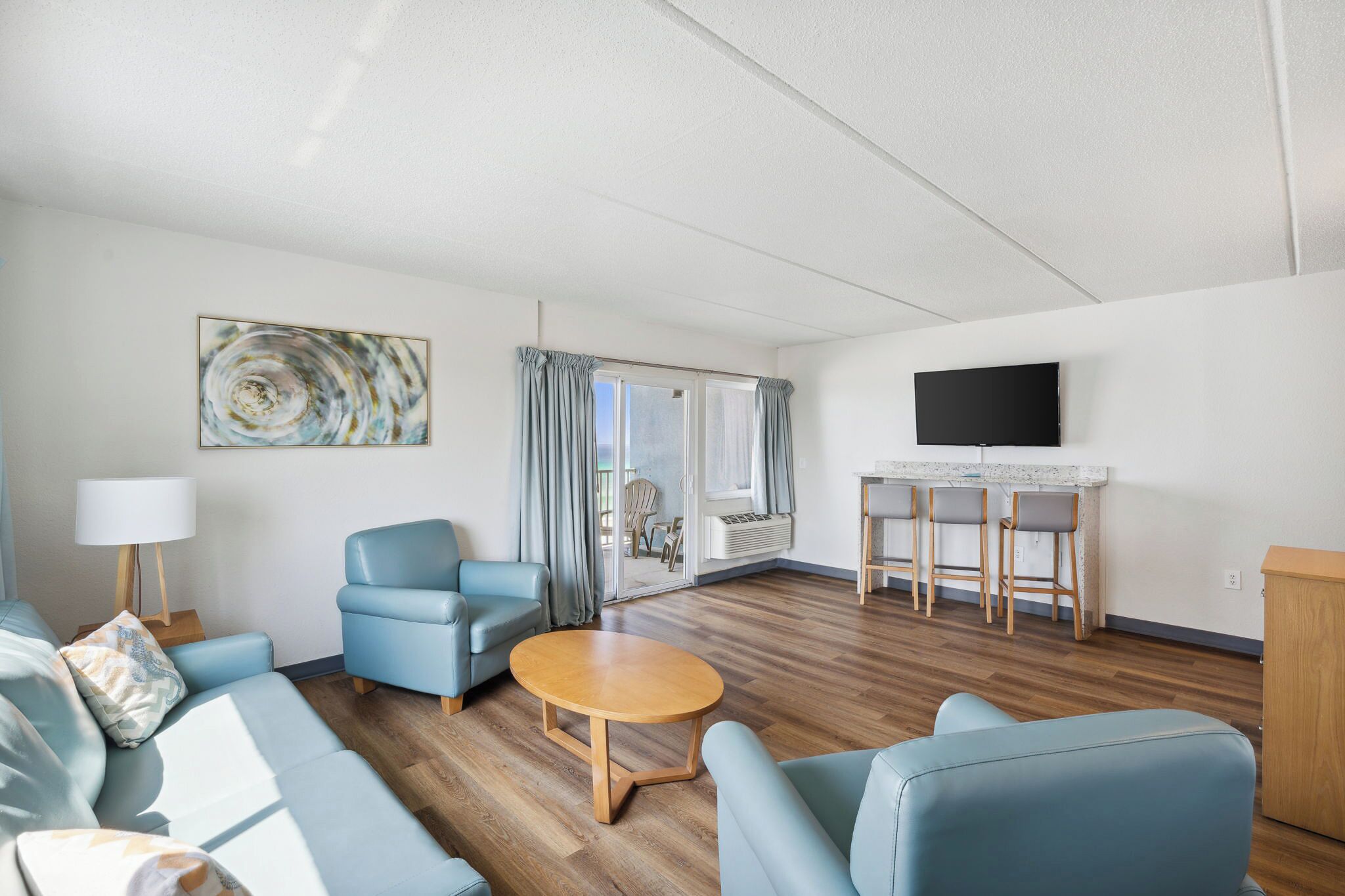 Un salon moderne comprenant un canapé, un fauteuil, une table ronde et un téléviseur fixé au mur.