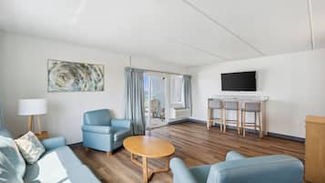 Un salon moderne comprenant un canapé, un fauteuil, une table ronde et un téléviseur fixé au mur.