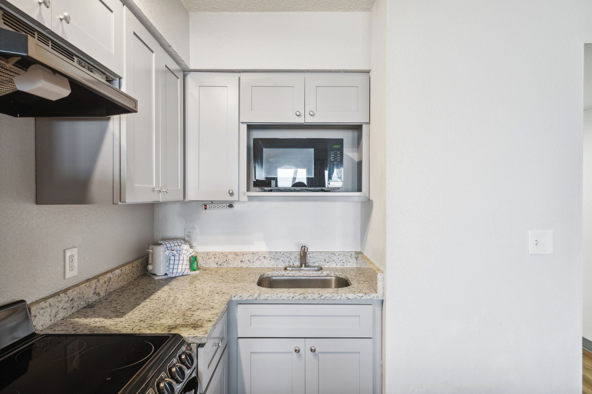 A compact kitchen with white cabinets, a microwave, a sink, and a stove.