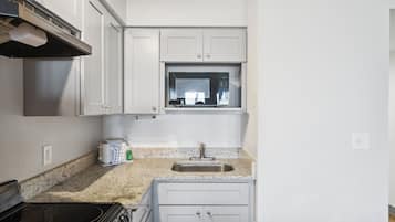 A compact kitchen with white cabinets, a microwave, a sink, and a stove.