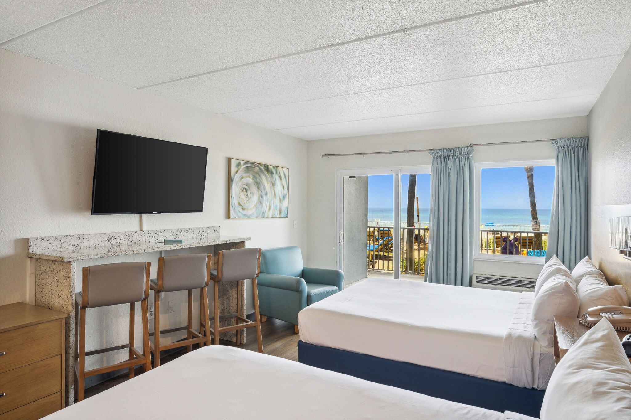 Habitación de hotel con televisión, obras de arte, balcón con vistas, escritorio y sillas, y una cama.
