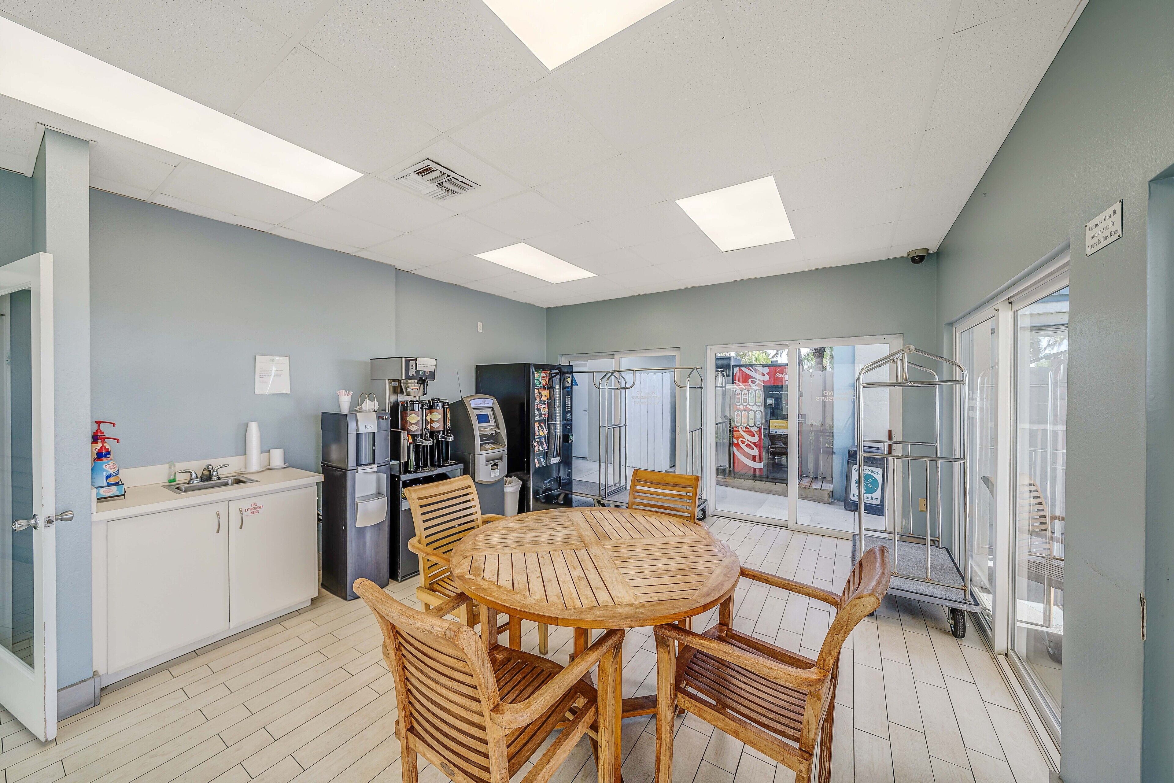 A dining area with a round wooden table and chairs, a refrigerator, a coffee machine, and a vending machine.