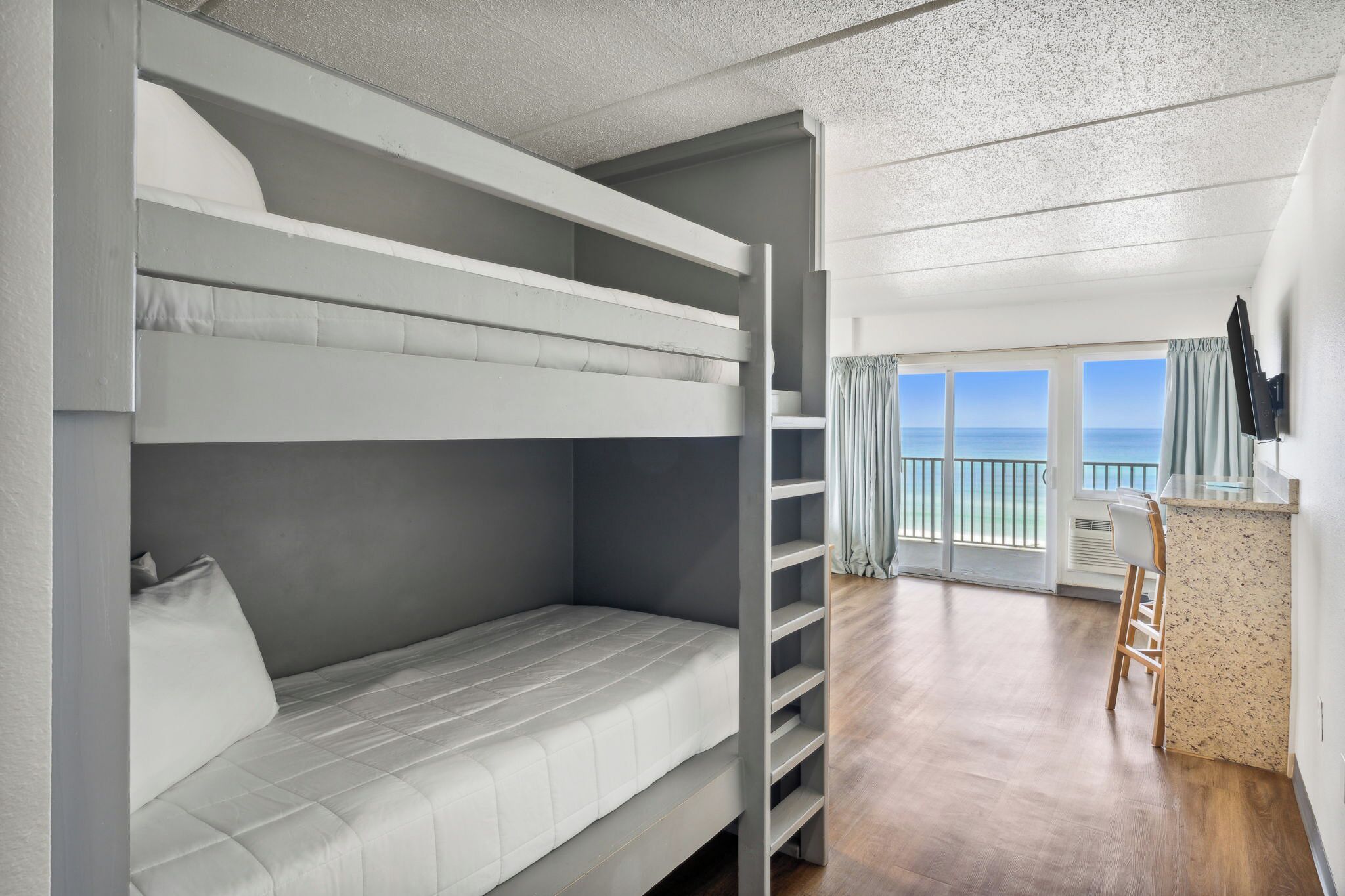 A bunk bed room with a view of the ocean, a bar area, and a large window.
