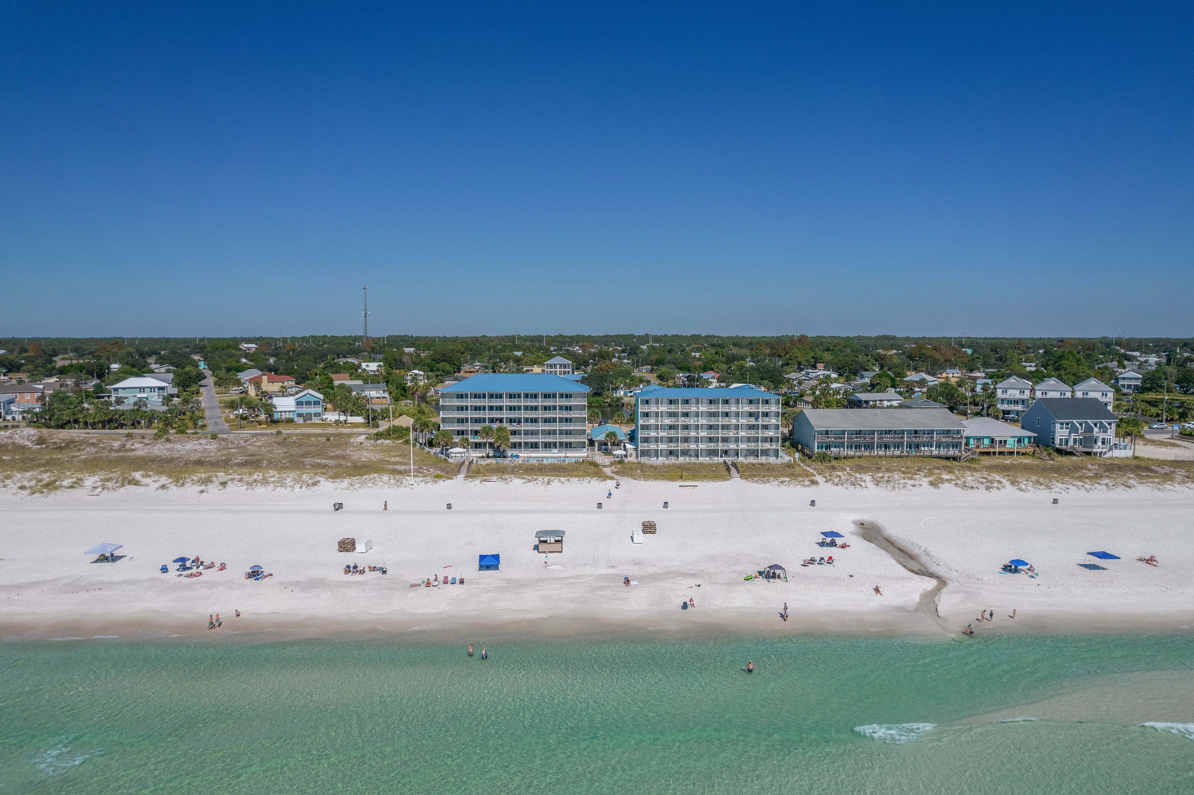 A coastal hotel with multiple buildings, a sandy beach, and clear turquoise waters.