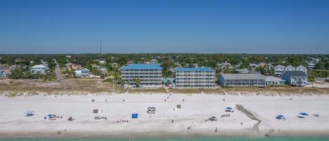 Un hotel costero con varias construcciones, una playa de arena y aguas turquesas cristalinas.