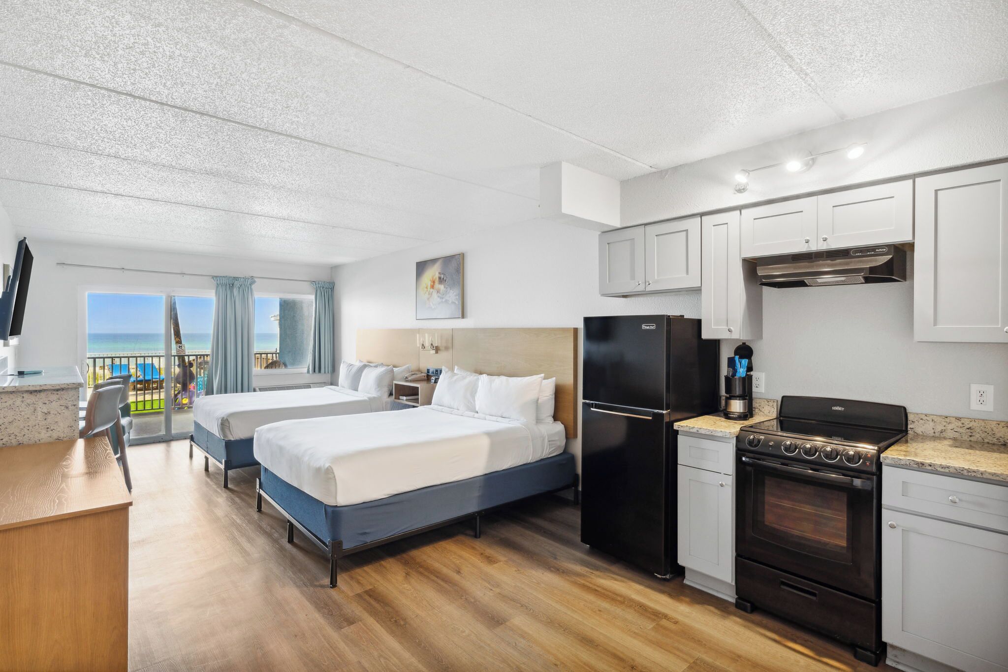 A hotel room with two beds, a kitchenette, and a balcony with a view.