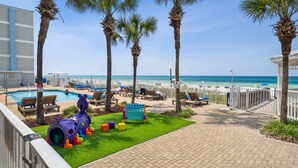 A pool area with lounge chairs, palm trees, and a children's play structure.
