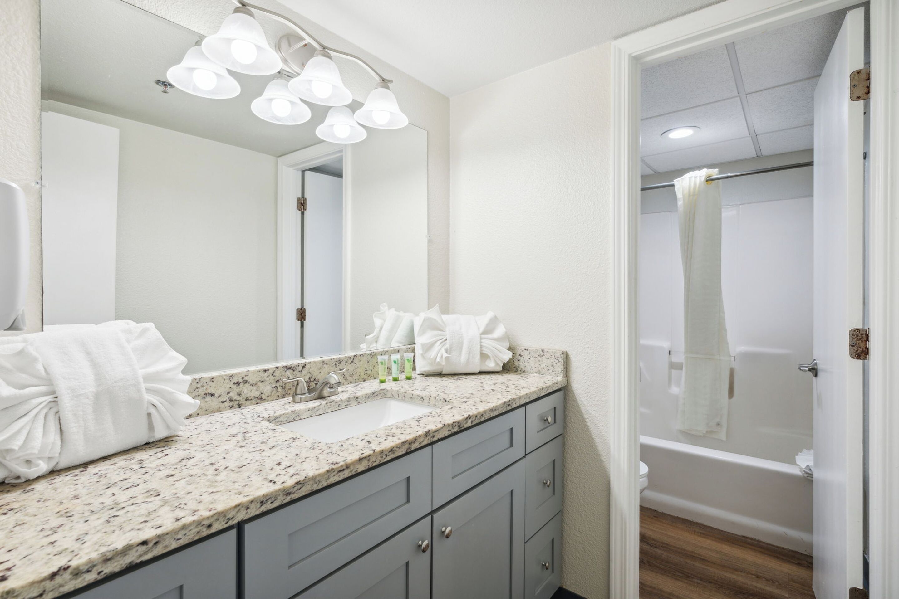 A bathroom with a granite countertop, a sink, a mirror, and a shower area.