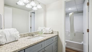 A bathroom with a granite countertop, a sink, a mirror, and a shower area.