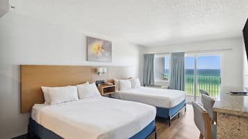 Habitación de hotel con dos camas, un escritorio, una silla, un cuadro y un balcón con vistas.