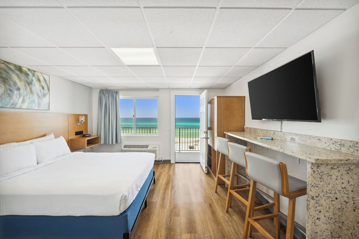 Habitación de hotel con cama, escritorio con televisor, balcón con vistas y ventana.