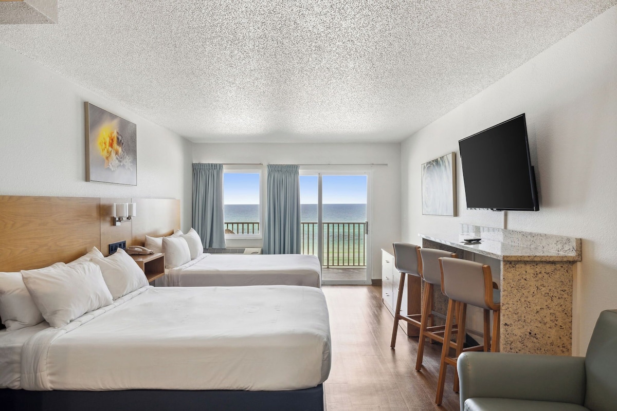 Een hotelkamer met twee bedden, een bureau, een televisie en een balkon met uitzicht.