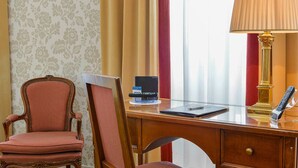 A hotel room with a wooden desk, a striped chair, a lamp, a remote control, and a laptop. - Albergo Alla Posta (Trieste)