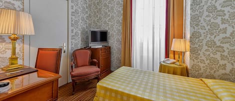 Habitación de hotel con escritorio de madera, televisor, cama con colcha a cuadros y una pequeña mesa con lámpara.