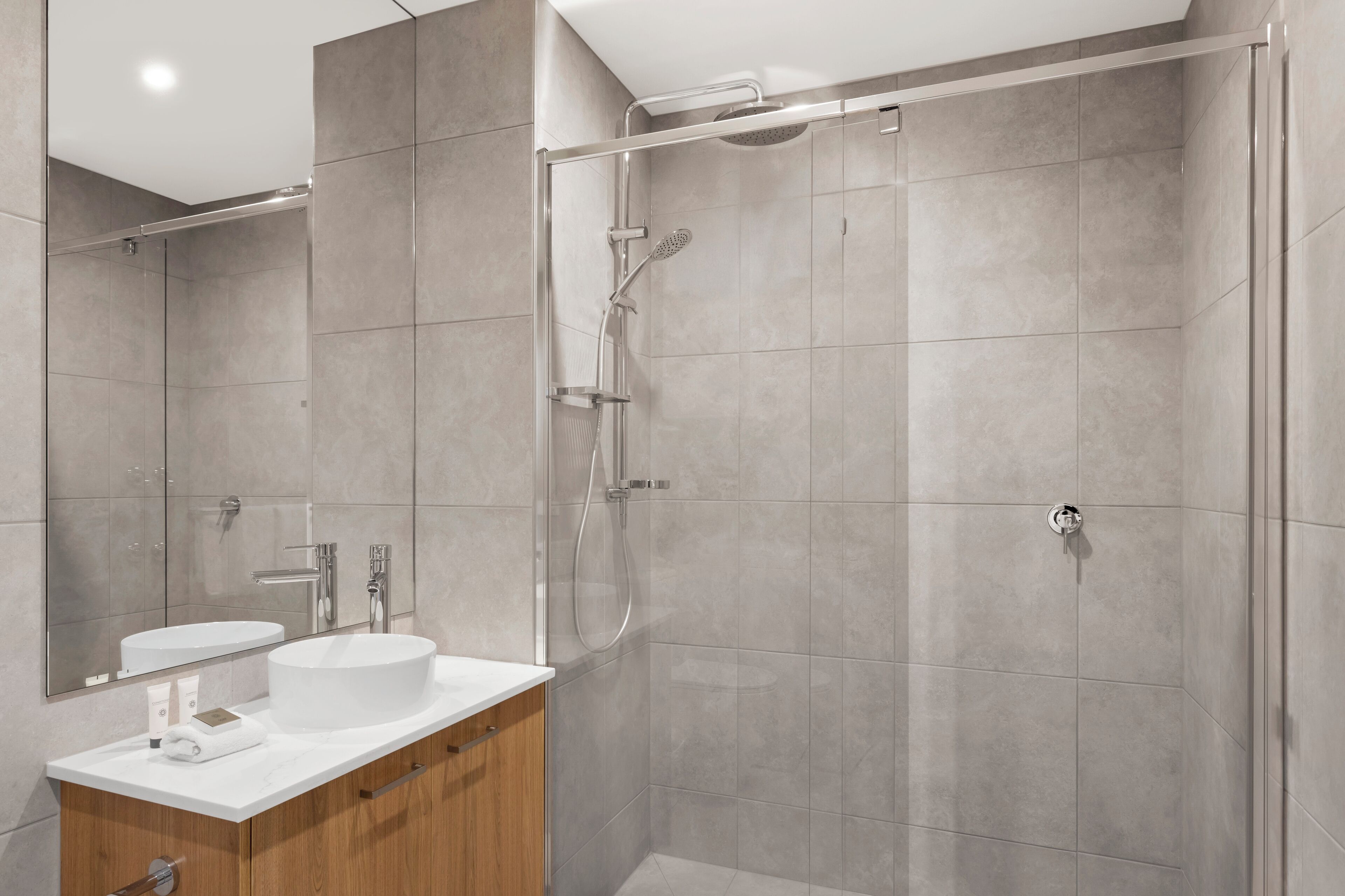 A modern bathroom with a glass-enclosed shower, a white sink, and a wooden vanity.