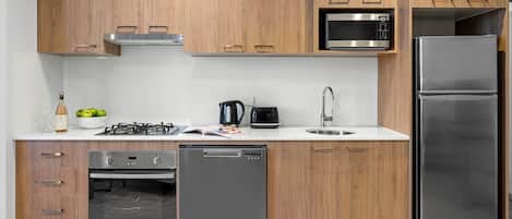 A modern kitchen with wooden cabinets, stainless steel appliances including a microwave, gas stove, dishwasher, and refrigerator.