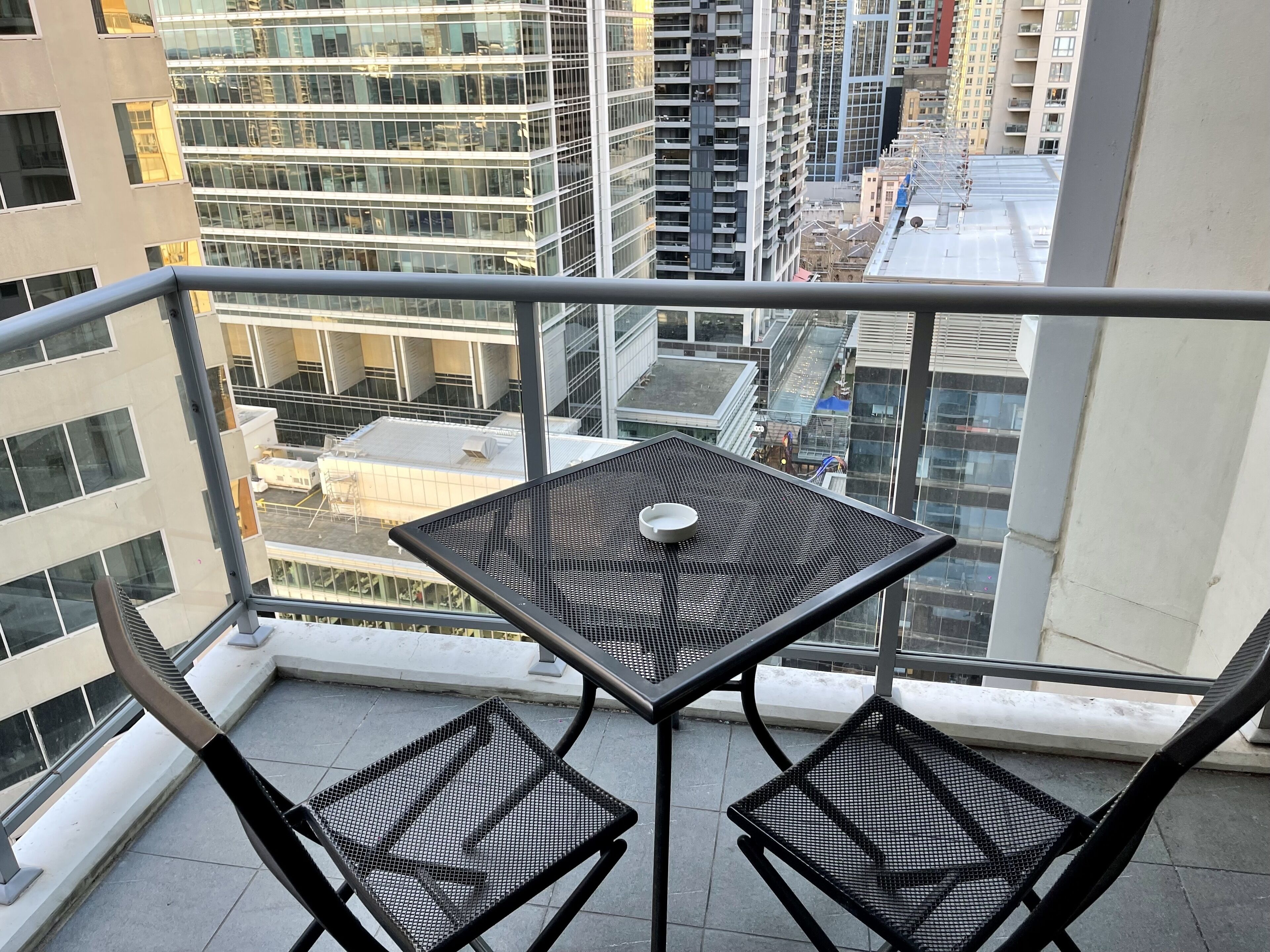 A balcony with a table and two chairs, overlooking a cityscape with high-rise buildings.