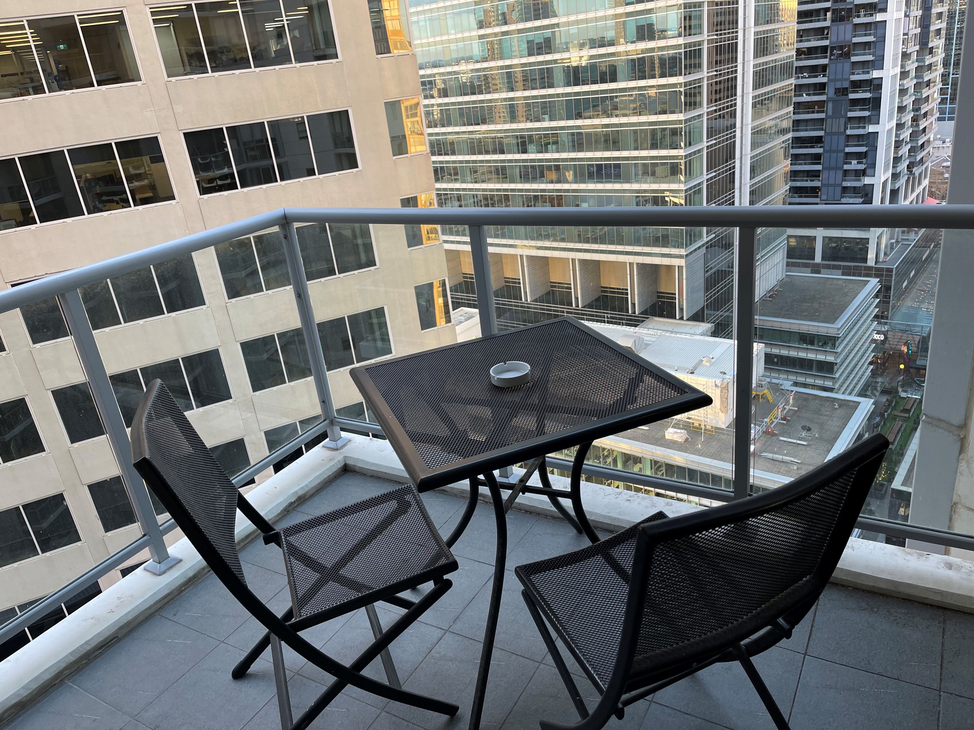 A balcony with a table and two chairs, overlooking a cityscape with modern buildings.
