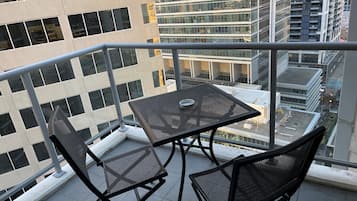 Un balcon avec une table et deux chaises, donnant sur un paysage urbain avec des bâtiments modernes.