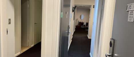 A hotel corridor with a carpeted floor, a door on the left, and a sign on the right wall.