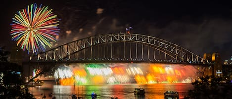 Eine Brücke mit farbenprächtiger Lichtinszenierung und Feuerwerk im Hintergrund.
