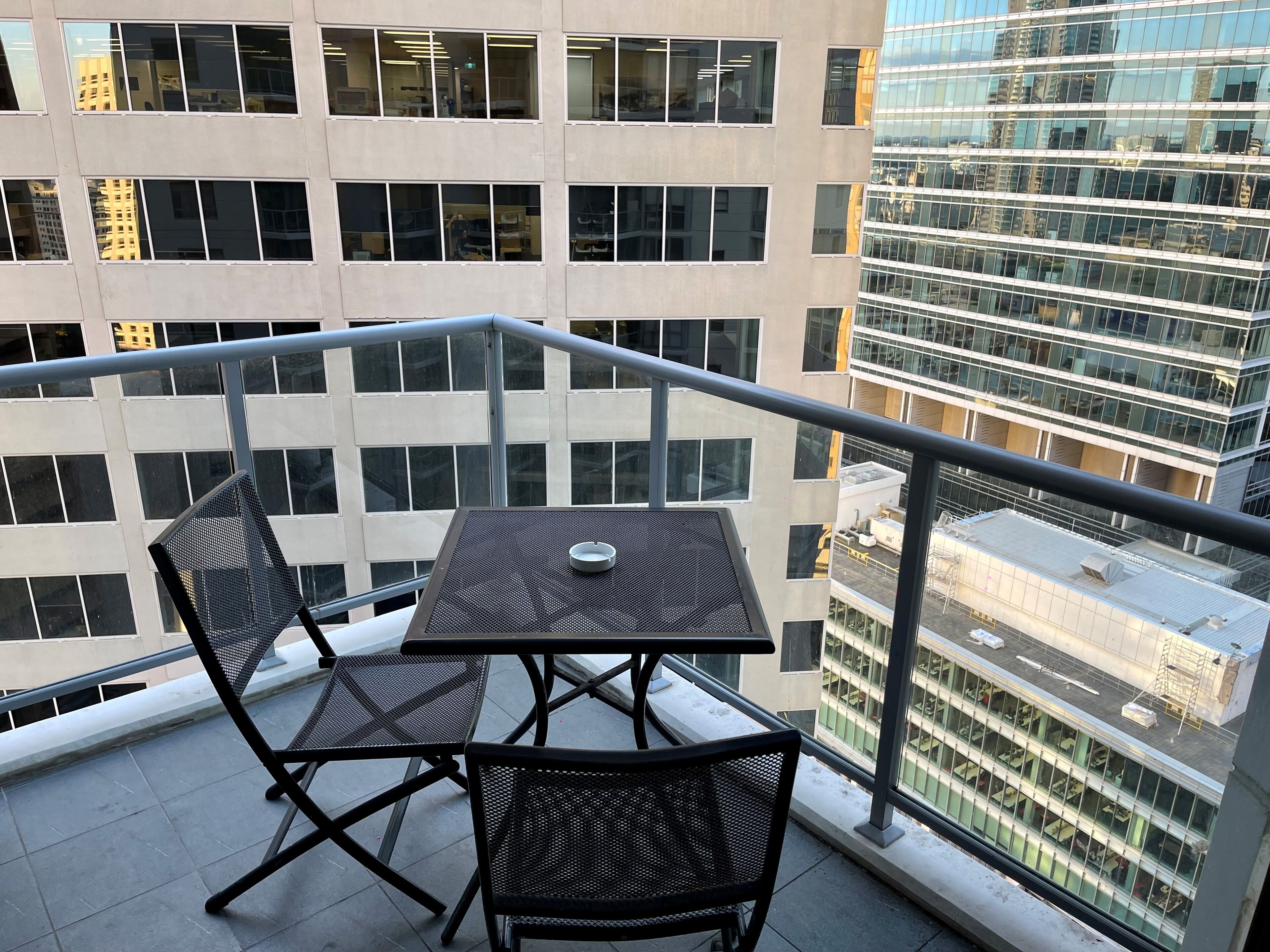 A balcony with a table and chairs, overlooking a cityscape with modern buildings.