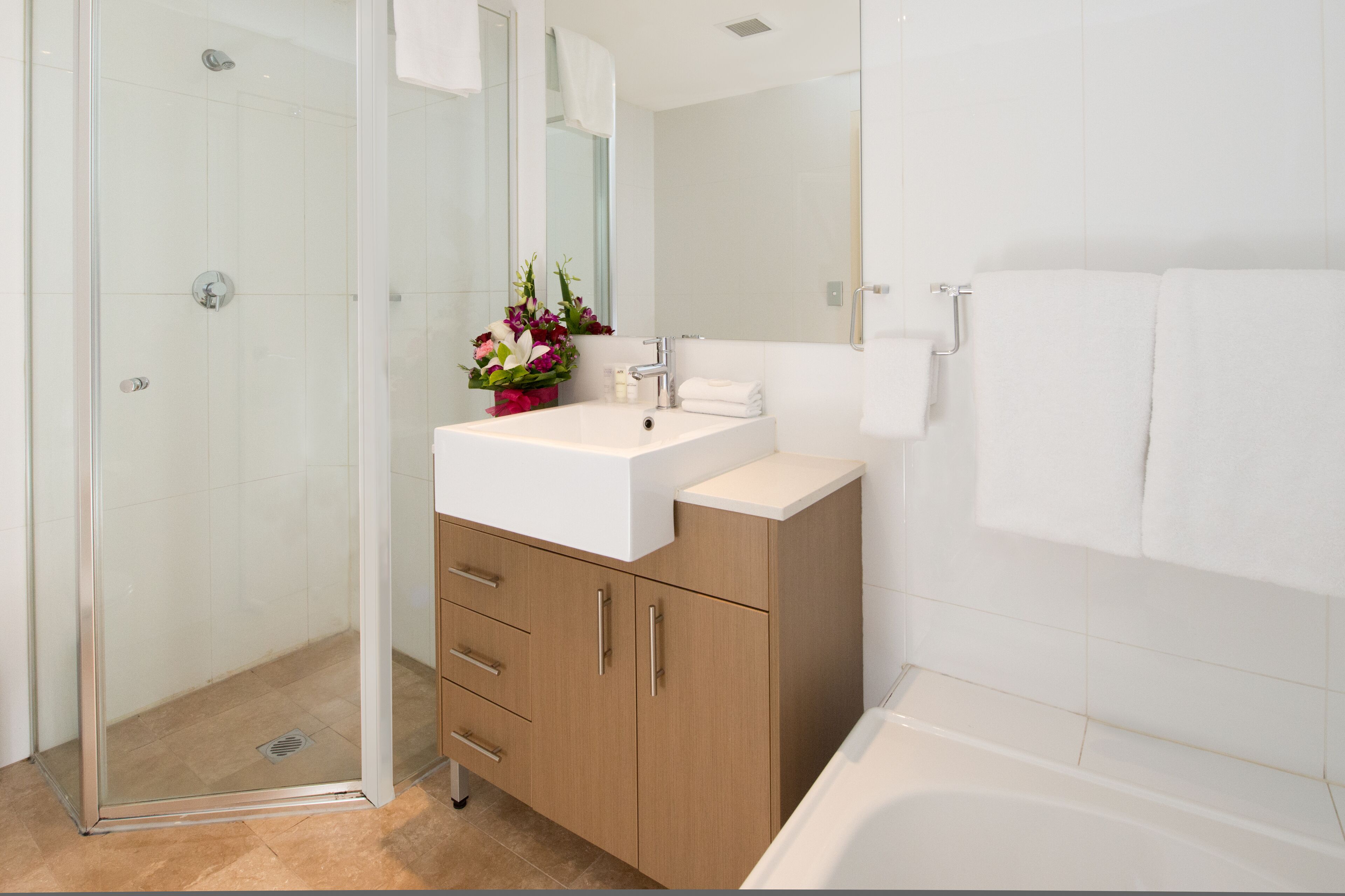 A modern bathroom with a glass shower enclosure, a white sink with a mirror above, and a bathtub.