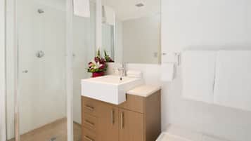 A modern bathroom with a glass shower enclosure, a white sink with a mirror above, and a bathtub.