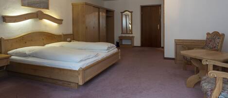 Un dormitorio con una cama de madera, un armario de madera, un espejo y una mesa de madera con una silla.
