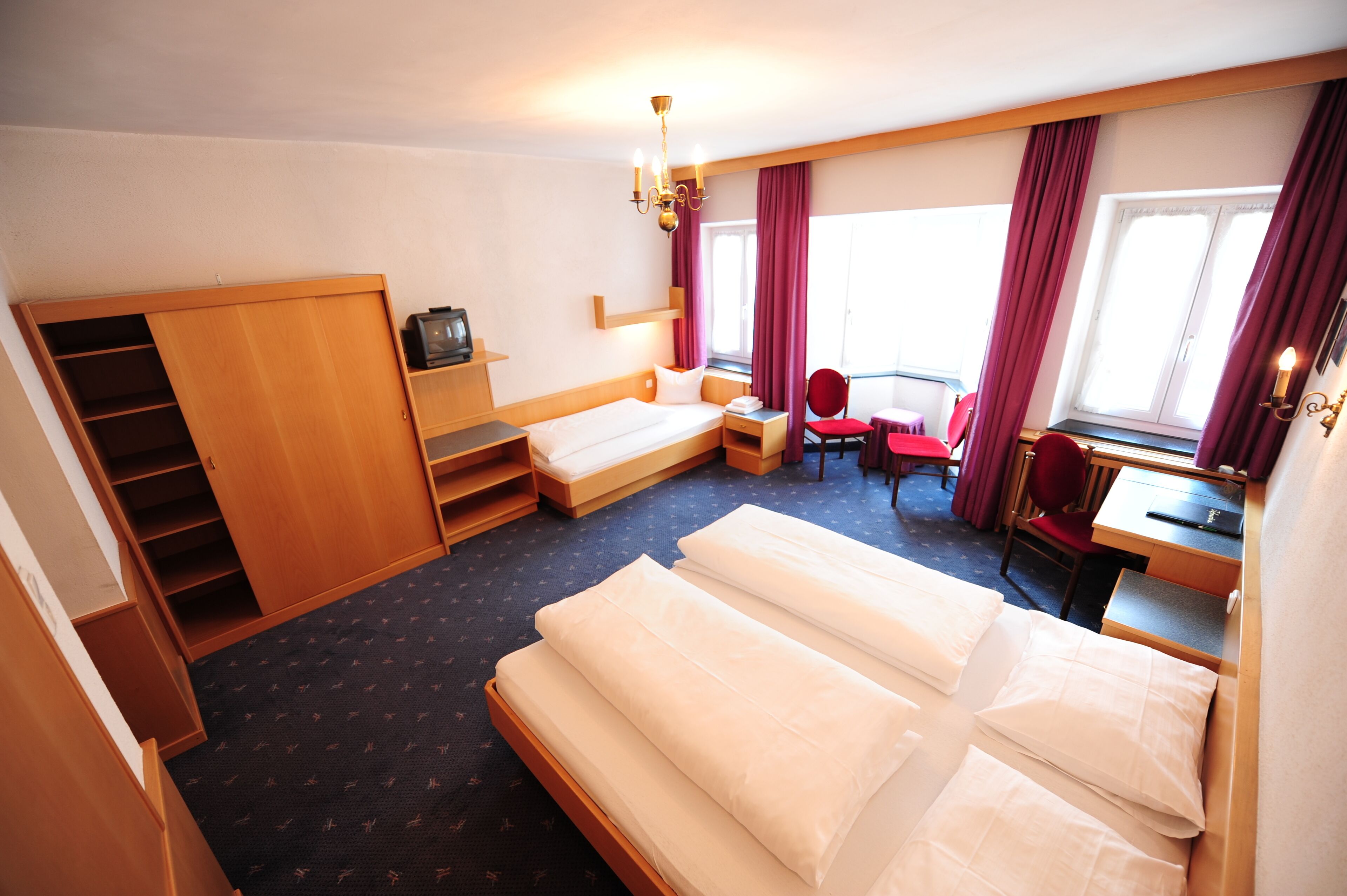 Una habitación de hotel con cama, escritorio, silla, televisor y armario.