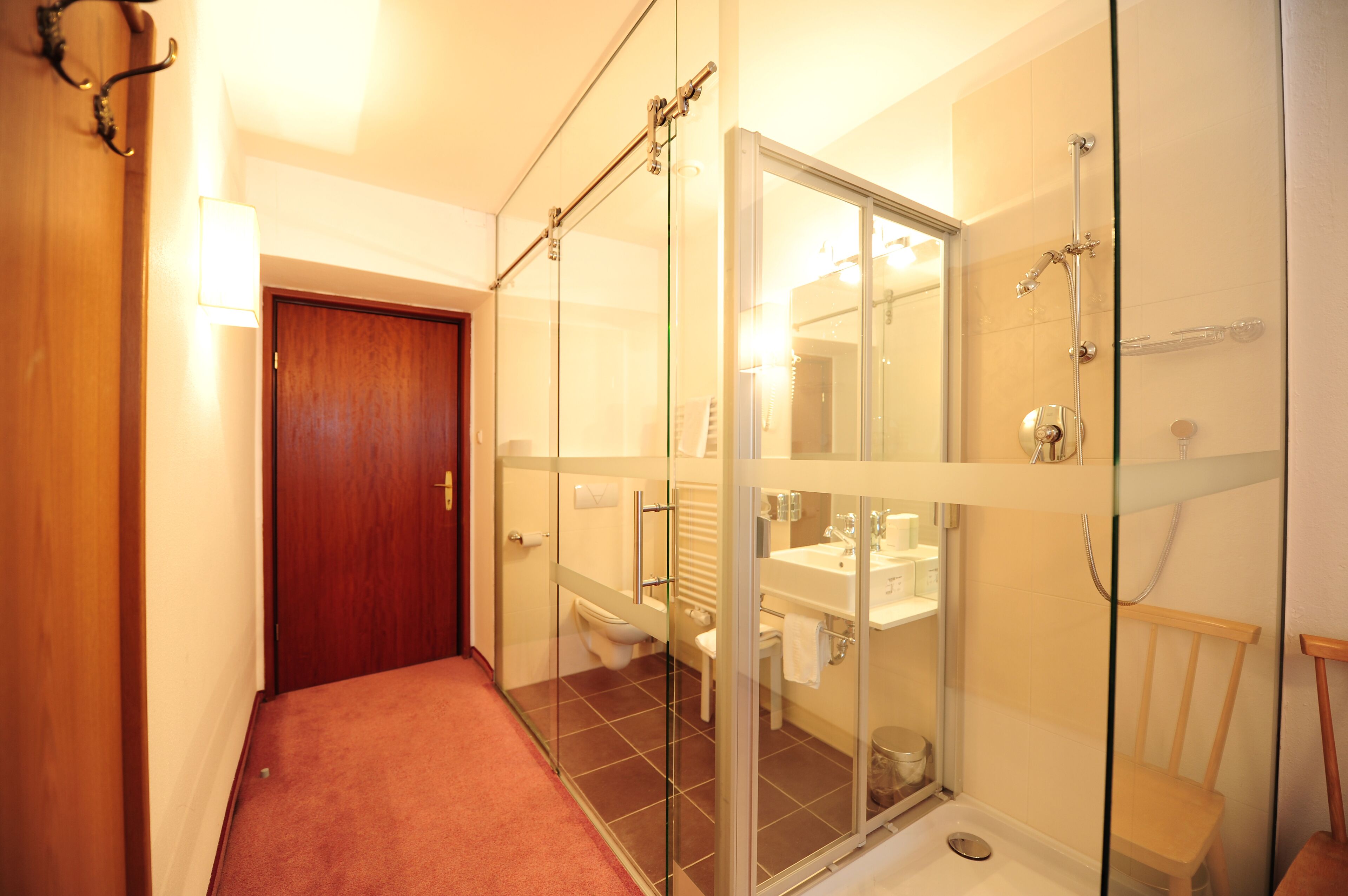 Un baño moderno con cabina de ducha de vidrio, puerta de madera y un inodoro a la vista.