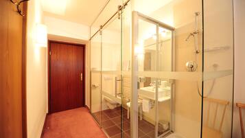 Un baño moderno con cabina de ducha de vidrio, puerta de madera y un inodoro a la vista.