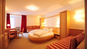 A hotel room with a round bed, a small desk, a chair, a sofa, and a cabinet. - Hotel Krone (Matrei am Brenner)