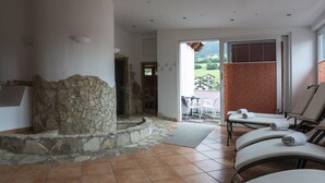 A spa area with a stone fireplace, a massage table, and a view of the outdoors. - Hotel Krone (Matrei am Brenner)