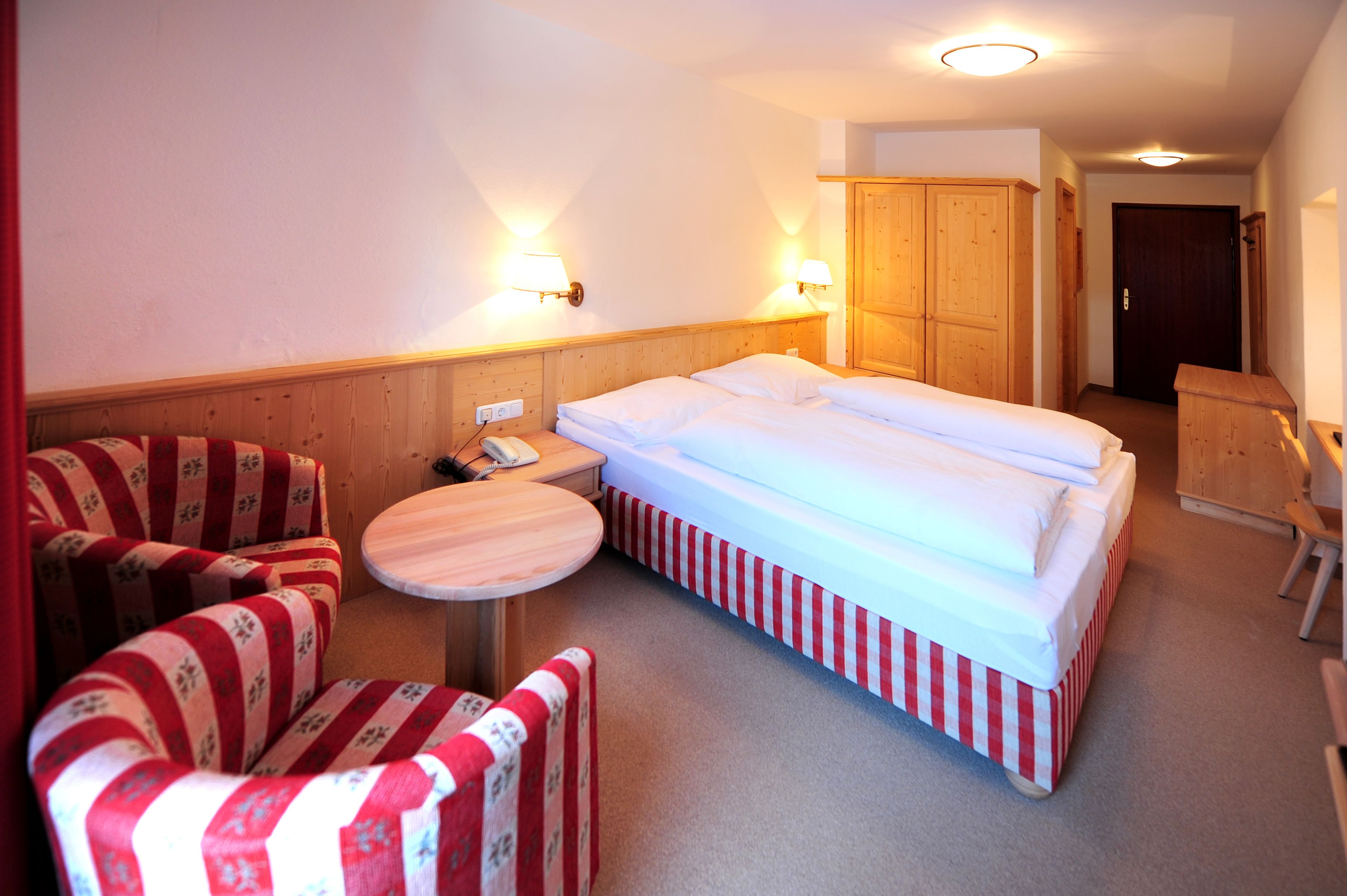 A hotel room with a bed, two chairs, a small table, and a wooden wardrobe.
