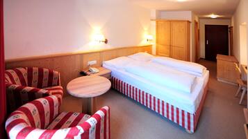 A hotel room with a bed, two chairs, a small table, and a wooden wardrobe.
