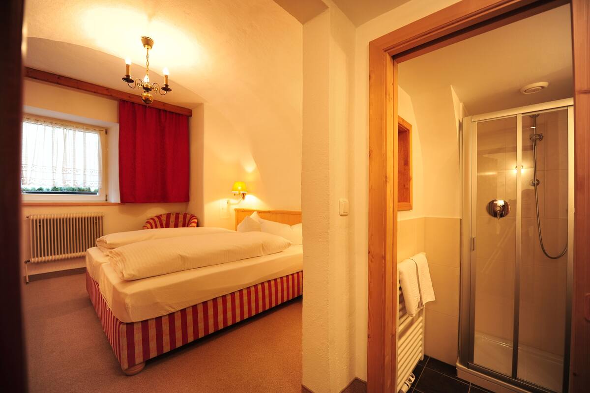 A hotel room with a bed, a shower, a window with curtains, and a radiator.
