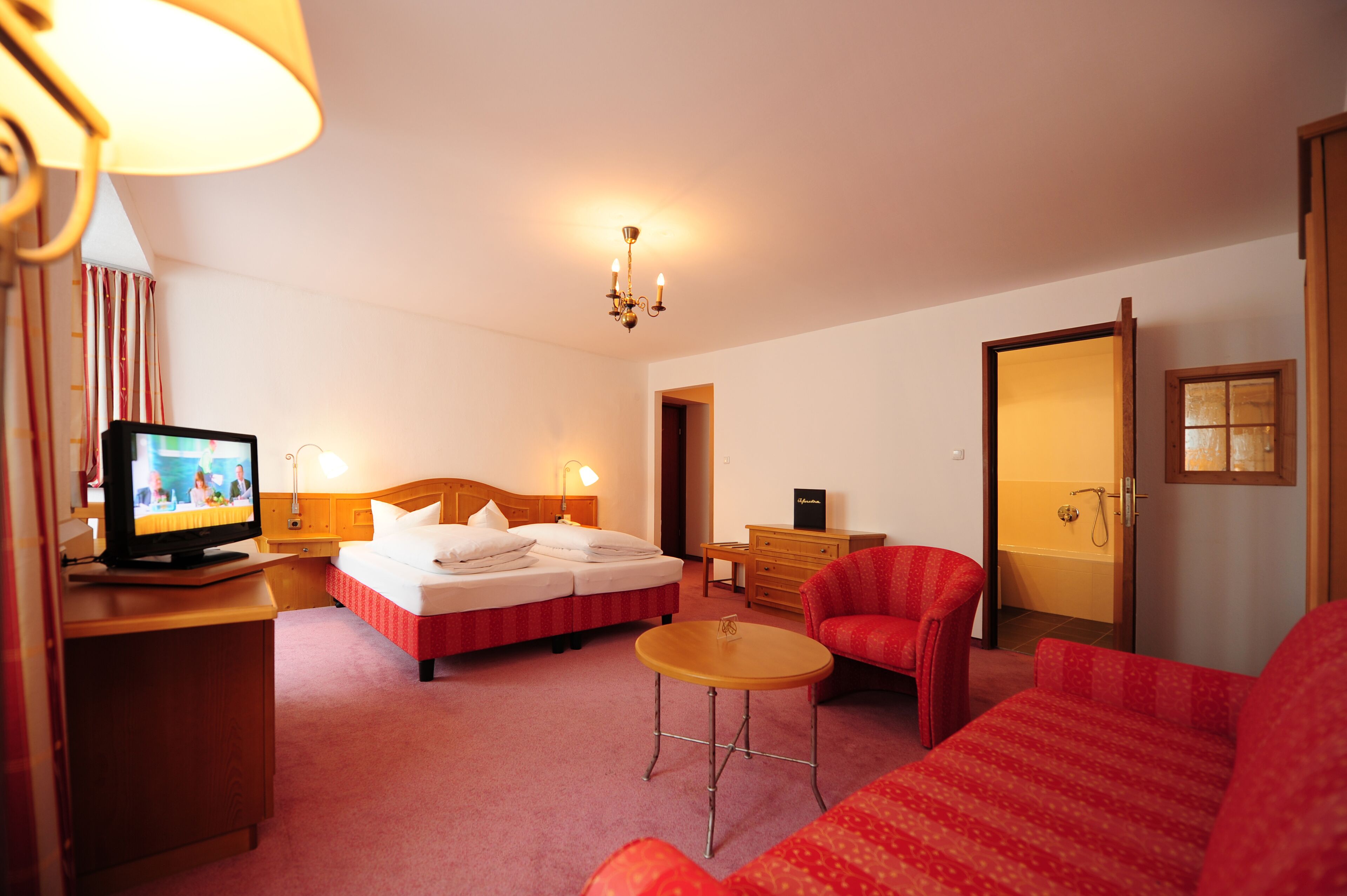 A hotel room with a bed, a TV, a desk, a chair, and a bathroom door.