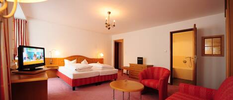 A hotel room with a bed, a TV, a desk, a chair, and a bathroom door.