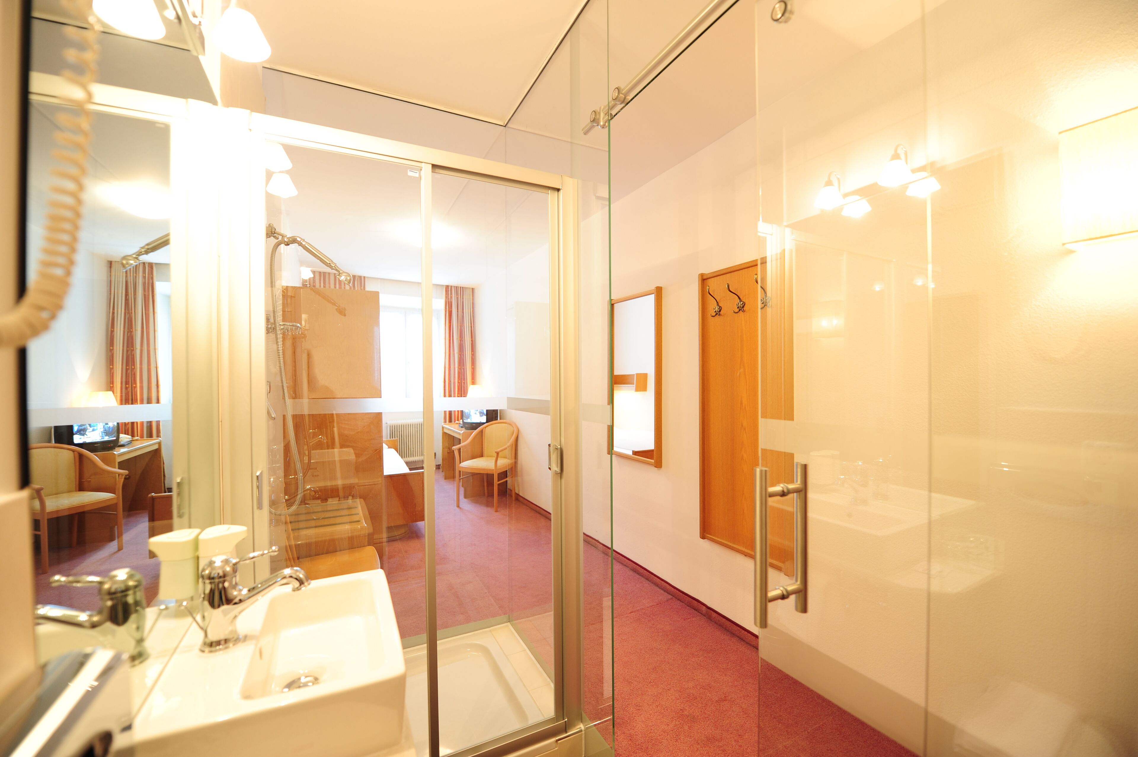 A hotel bathroom with a glass shower enclosure, a sink, and a mirror.
