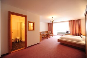 Une chambre d’hôtel comprenant un lit, un coin salon avec une table et des chaises, une télévision, ainsi qu’une salle de bain avec douche et toilettes.