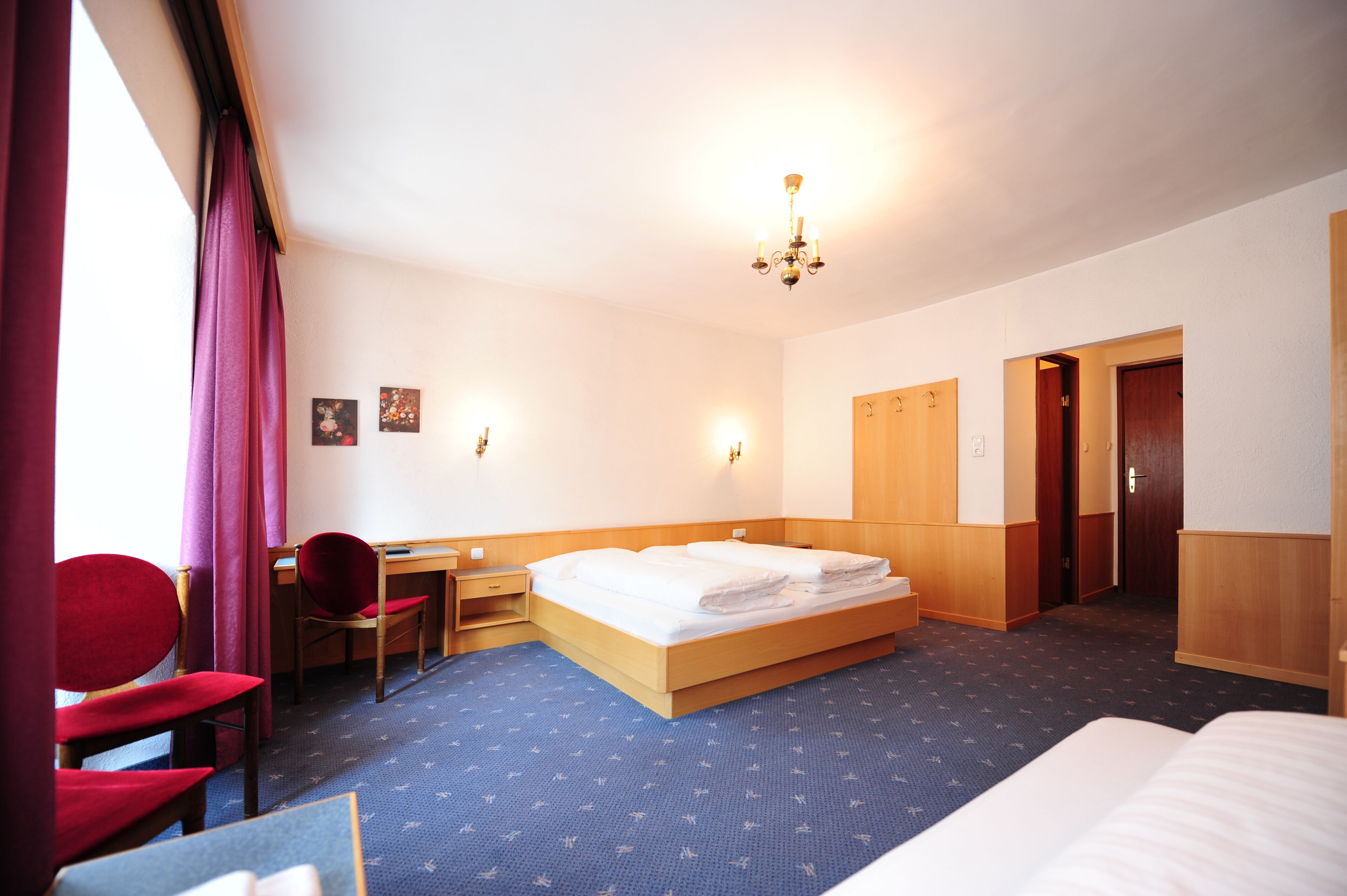 A hotel room with a bed, a desk, a chair, and a wardrobe.